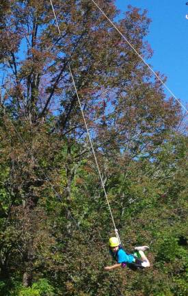 A student is shown high above the ground and swinging from the rope on the Flying Squirrel segment.