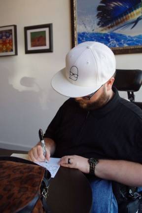 D'Agostino holds poetry reading at Art Etc. Nicholas D'Agostino is shown autographing a copy of his poetry collection book "Inside Out." His distinctive logo is featured on his white ball cap.