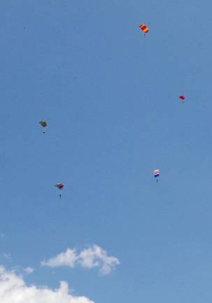 Five skydivers can be seen near each other above the south field at Sussex Airport.