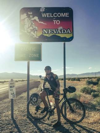 Vernon residnet biking for MS awareness Jeff Brath poses in front of a sign at the Nevada border heading west.