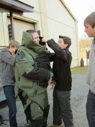 Crew members help Treasurer Thomas Seltzer put on a bomb suit.