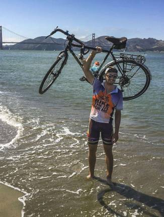 Vernon residnet biking for MS awareness Jeff Brath holds the bicycle over his head at the Pacific Ocean.