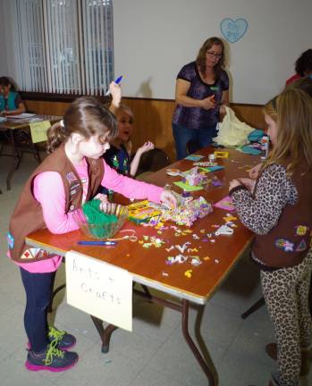 Girls work at the crafts table. In the background is girl scout leader Suzette Houdershieldt.