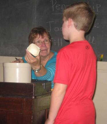 Vernon Historical Society member and retired Vernon teacher Nancy Adam shows visitor Shawn Damstra how past students received water in school.