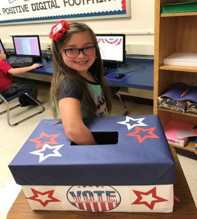 A 3rd grade student places her signed registration ticket into the box before casting her online vote.
