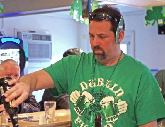 Wearing green leprechaun ears, bartender Tim Kenney pours a drink.