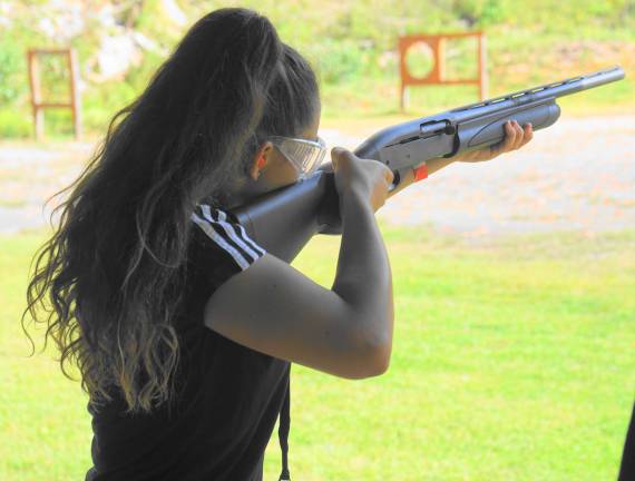 A young woman shoots shotgun at flying clay birds.