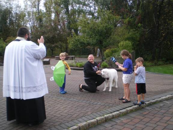 Father Chris Barkhausen, pastor of St. Francis de Sales Church in Vernon, blesses Coco, a dog owned by the MacIntosh family, at the annual blessing of the animals honoring the Feast Day of St. Francis of Assisi on Saturday, Oct. 7. (Photo by Janet Redyke)
