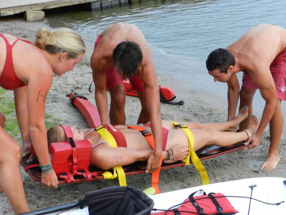 LMCC Lifeguards Megan Howson, Mark and Jack Donahue strap in &quot;victim&quot; Liz Zanetakos.