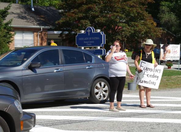 Two ladies collect donations from cars passing by Our Lady of Fatima Church in Highland Lakes.