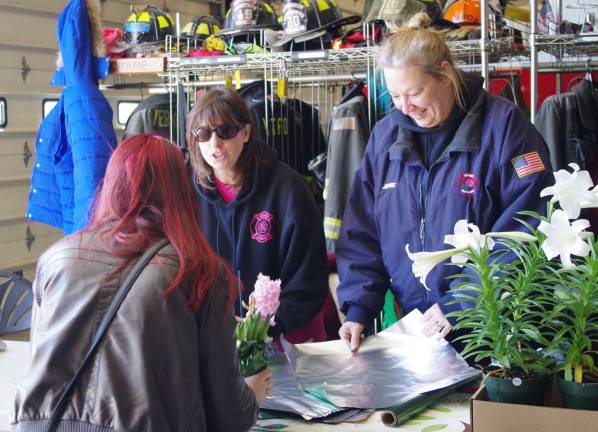 Behind the table are Vernon Fire Department Ladies Auxiliary members Kareen Alba and Jennie Della Torre shown helping a customer with her flower purchase.
