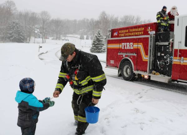 PHOTOS BY MARK LICHTENWALNERA Vernon Township firefighter hands a child a candy cane on Saturday as Santa looks on from the fire truck.