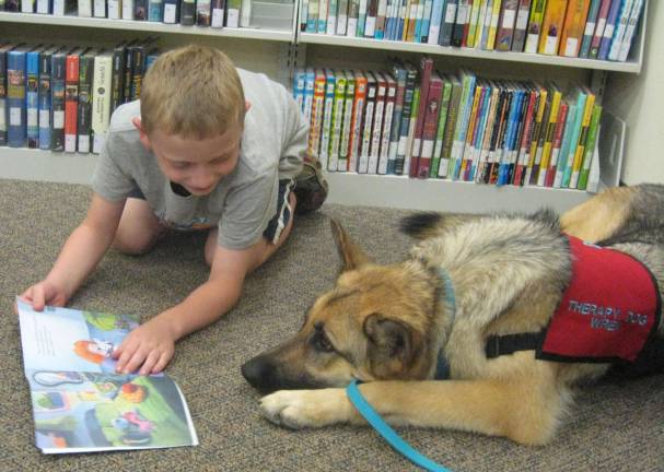 Therapy dog visits library Gaius Hanson explains a picture to the interested dog.
