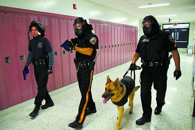 Vernon police train for the worst Photos by Chris Wyman With weapons drawn, three Vernon Township police officers and police dog “Hobbs” walk down a hall in the high school while looking for an armed gunman responsible for killing and wounding a yet unknown number of students.