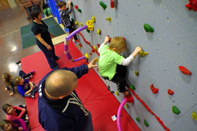 Physical education teacher Todd Piontkowski is shown guiding a kindergarten student across the face of the school&#x2019;s new Traverse Rock Climbing or &#x201c;Bouldering&#x201d; Wall.