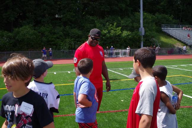 Children gather to punt, pass and kick Former N.Y. Giants running back Lee Rouson talks with youth on the field.
