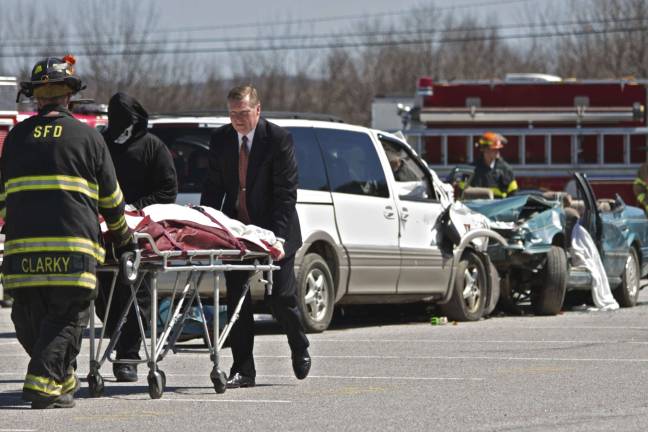 Staged fatal crash Firefighters, the Grim Reaper and a funeral home attendant cart away the body of the 'victim.'