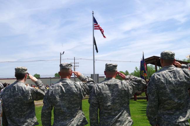 Army Reserve members saluting the flag as it is raised from half staff.