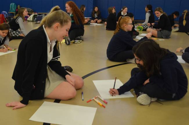 Pope John XXIII Regional High School senior Kayla Hannemann, left, watches Reverend George A. Brown Memorial School fourth grade student Giada Reali draw on her vision board during a Linking Lions meeting in December at Reverend George A. Brown Memorial School in Sparta.