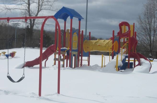 Playground equipment stands empty and childless in the snow.