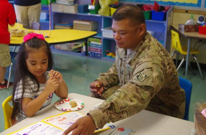 Army Sergeant First Class Roland Tajalle and his daughter Rai'Ana, 5, enjoy cookies in kindergarten teacher Connie Horn's classroom.