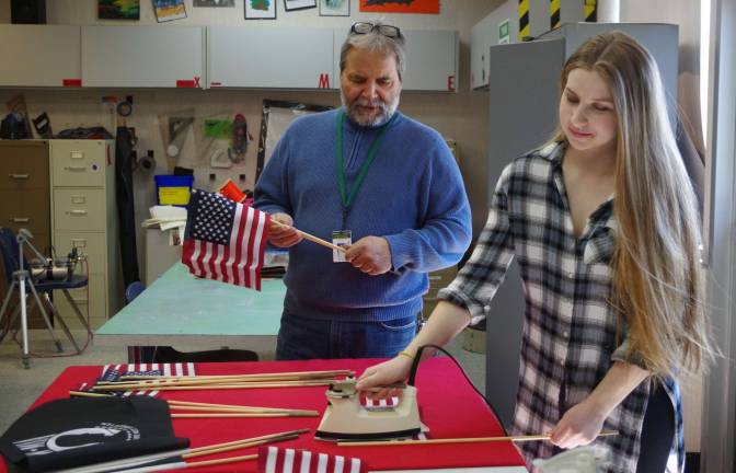 Event Coordinator/Commercial Art Instructor Dennis Paladini helps student Olivia Hayenhjelm, 17, of Lafayette prepare and iron the POW and American flags which supporters will purchase to be placed on the grounds during the show.
