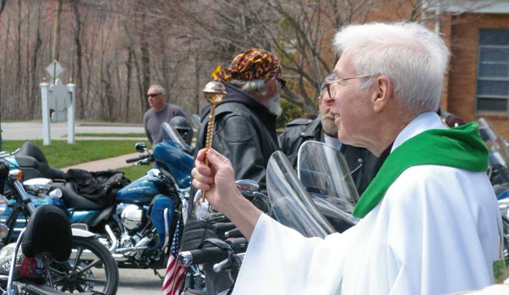 Monsignor Robert Carroll blesses the motorcycles by sprinkling holy water on the motorcycles and their riders.