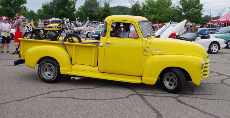 A classic yellow Chevy pickup truck hauling a color coordinated motorcycle is on the move.