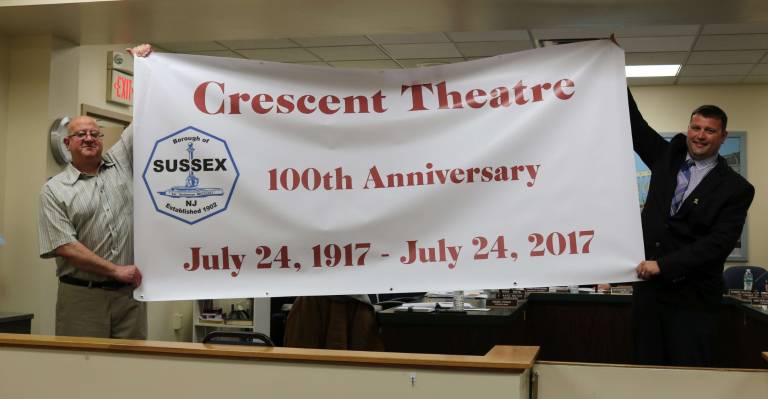 Council Member Mario Poggi (left) and Michael Restel hold up a Banner commemorating the 100th anniversary of the Crescent theater.