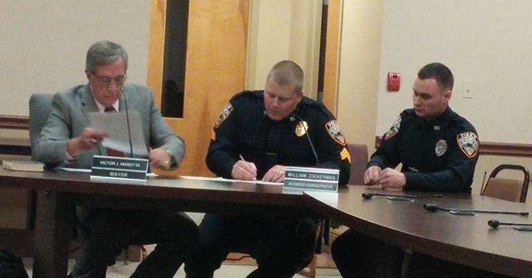 Newly promoted Vernon Township Police Sgt. David Dehart signs a sheet of paper as newly hired Officer Sean Pery looks on and Mayor Victor Marotta sits at left.