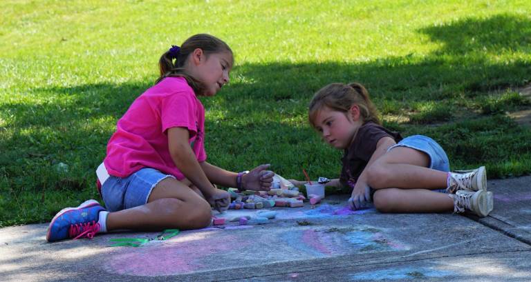 Two girls draw sidewalk chalk pictures.