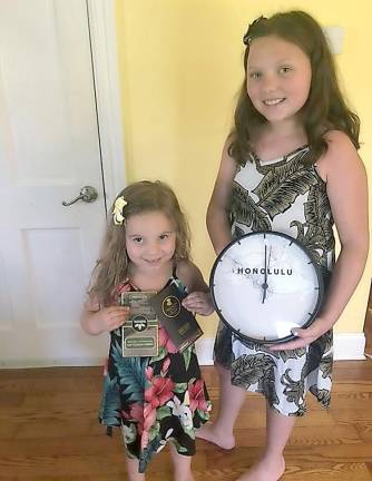 Regan and Brynn in their authentic Hawaiian dresses. Regan is holding chocolate from Hawaii and Brynn is holding a Honolulu clock so we always know the time in Hawaii.