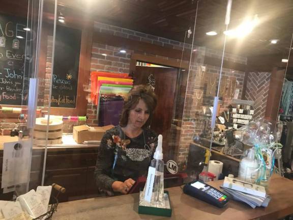 Janet Tikkanen, a vaccinated employee at Garlic &amp; Oil, works behind plexiglass barriers. The owner, Kathryn Kaplan, says “all our employees are vaccinated, but we keep masks around our necks in case a customer feels uncomfortable.”