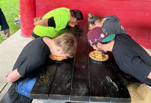 Four people compete in the pie-eating contest with their hands behind their backs.