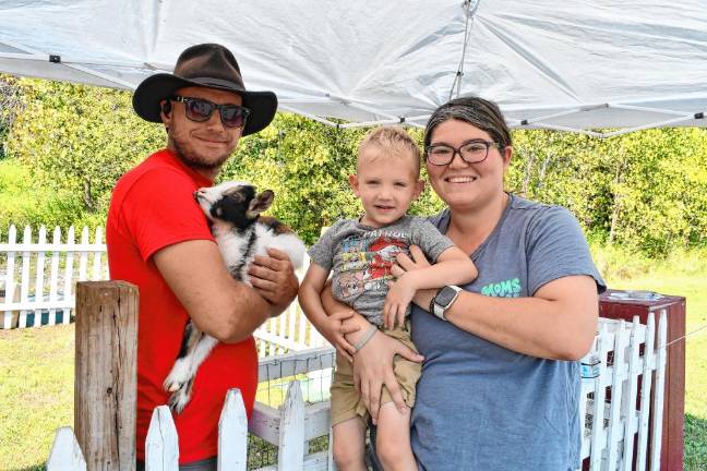 <b>Annmarie Crowe and Gage Myers of Vernon pose with a worker holding a goat at the petting zoo.</b>