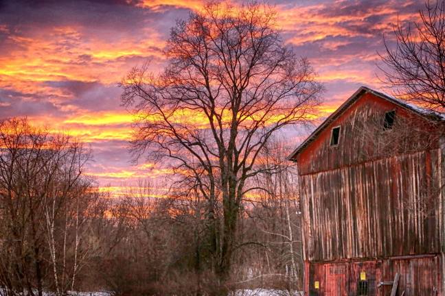 Photo by Gale Miko The sun is shown setting behind a barn in Wantage Township.