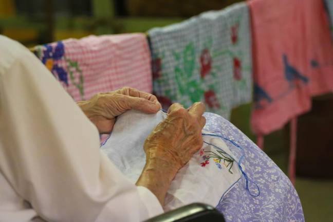 Seated beside a row of aprons made by her grandmother, Nan Horsfield patiently hand stitches wildflowers to her handkerchief.
