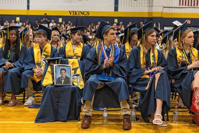 <b>Salutatorian James Bergacs sits next to a photo of Joseph Dunlop, a 2022 graduate who died June 8 at age 21.</b>
