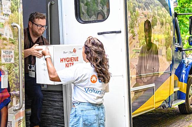 Volunteer Lindsay Benoza-Morales hands a box of hygiene kits packed by BD volunteers to Zufall fleet coordinator Jorge Castro for delivery to patients via the mobile unit.